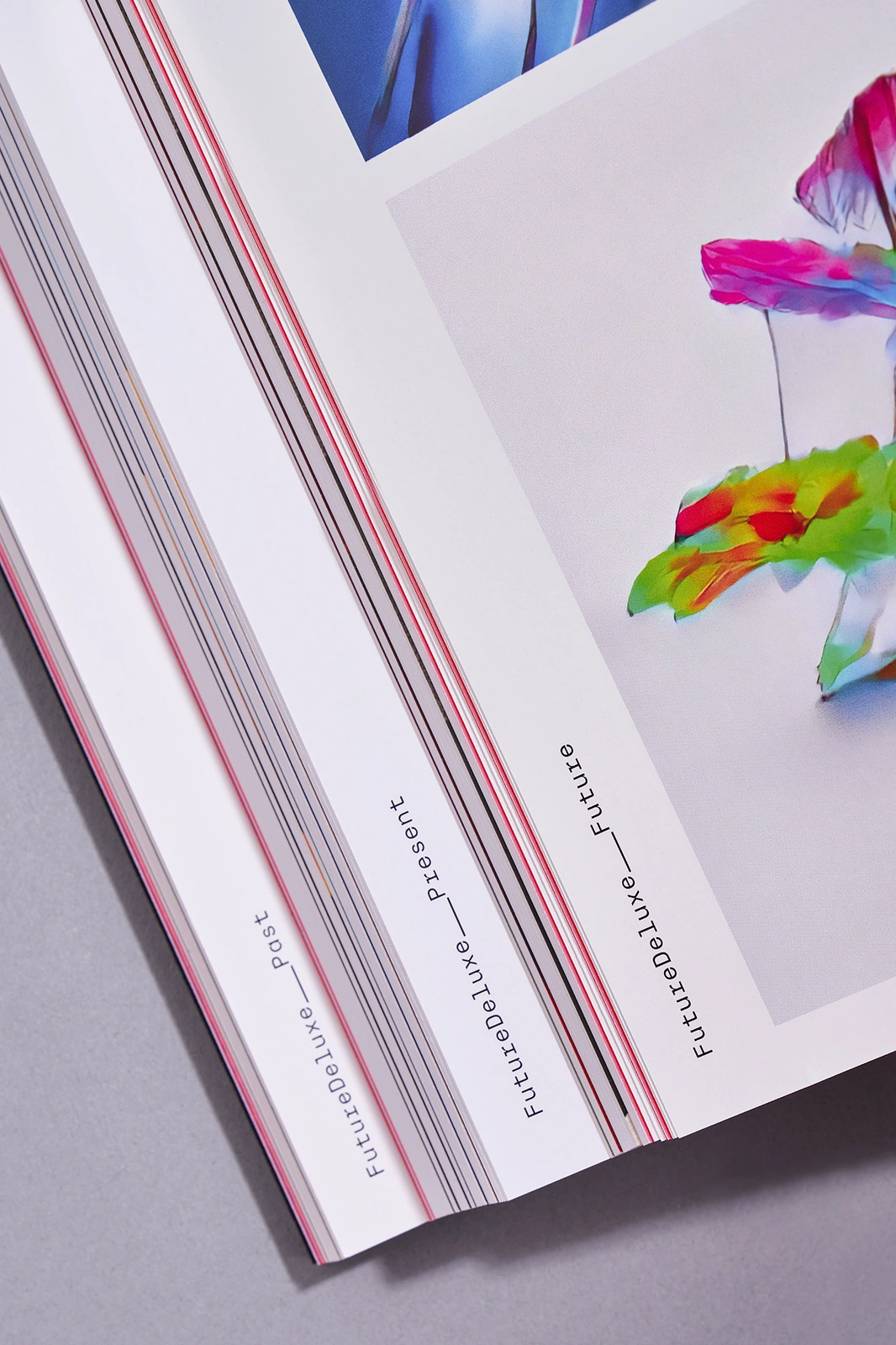 Close-up angled shot of open printed magazine pages featuring FutureDeluxe brand identity on white paper stock with colourful artwork.