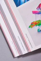 Close-up angled shot of open printed magazine pages featuring FutureDeluxe brand identity on white paper stock with colourful artwork.