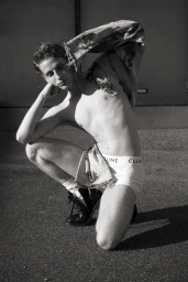Young man in white briefs and black boots crouching outdoors holding a distressed jacket for Markus Wiedemann