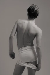 Rear view of a man with uncovered upper body wearing white briefs against a plain grey studio background.
