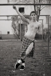 Shirtless man in plaid shorts holding onto an overhead metal bar in a playground setting