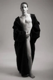 A shirtless male model wearing a draped black coat against a neutral grey studio background