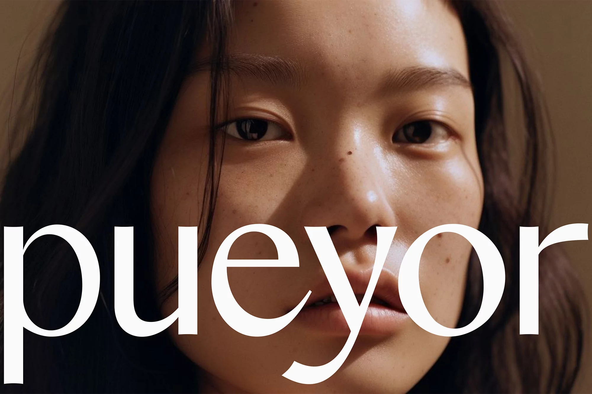 Close-up portrait of a young east asian woman with freckles and dark hair, overlaid with large white typography reading 'pueyor'.