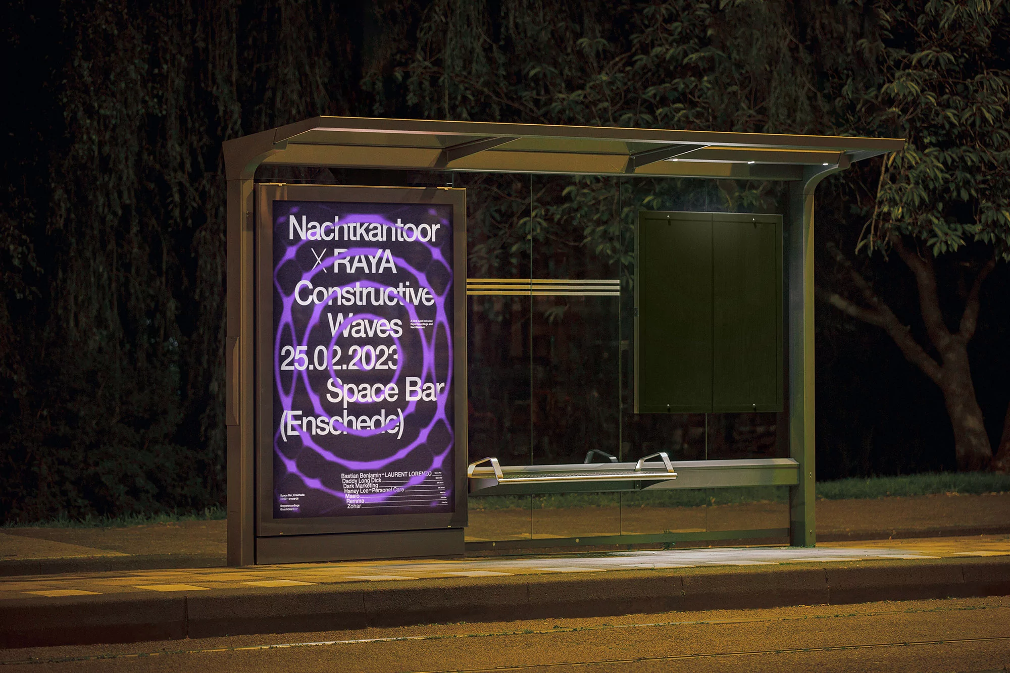 Bus stop ad at night displays Nachtkantoor X RAYA Constructive Waves event poster, urban setting, lit by streetlights, dark green foliage backdrop.