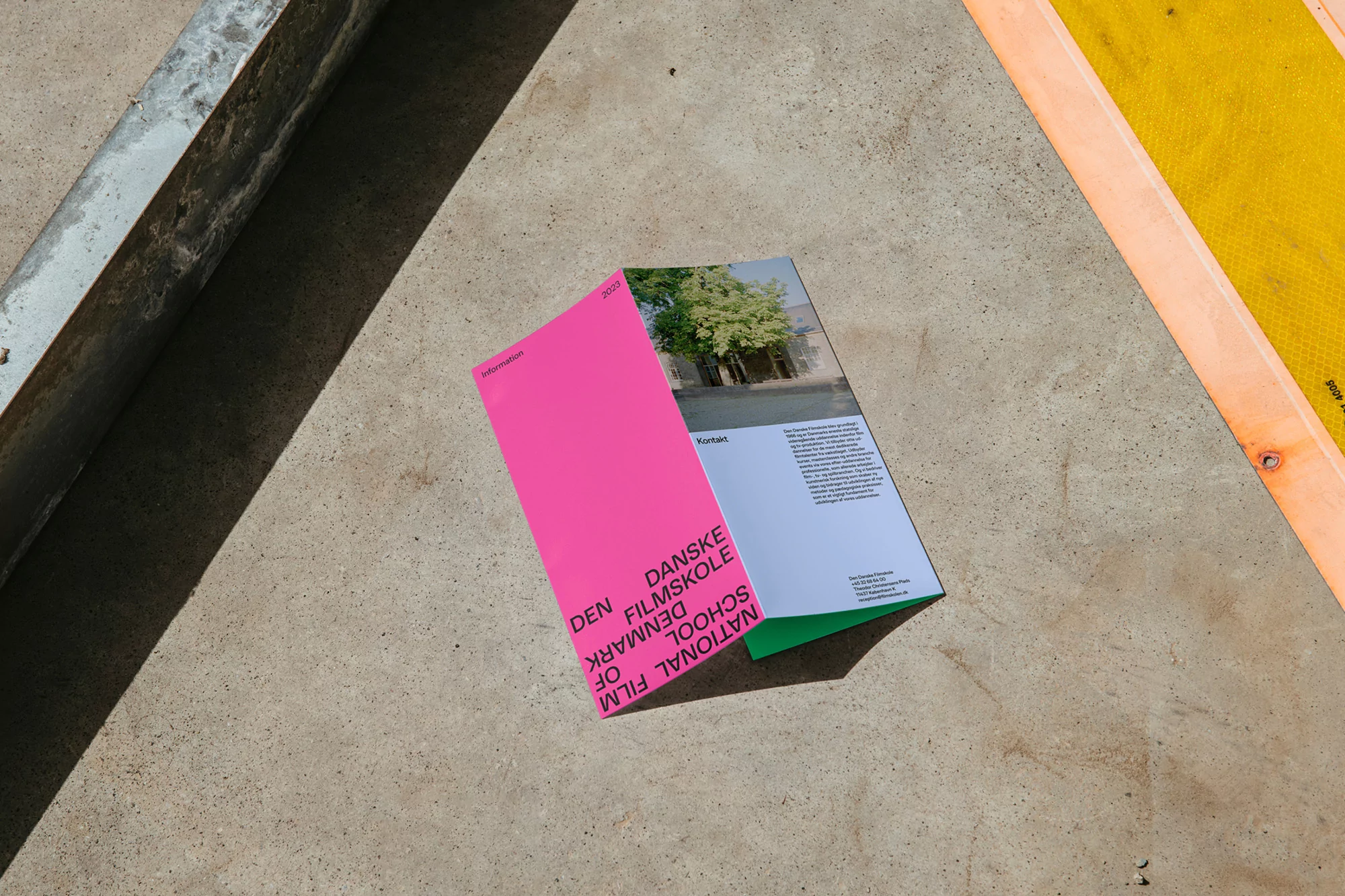 Promotional brochure for the Danish National Film School on a concrete surface, featuring school branding and an image on the cover.