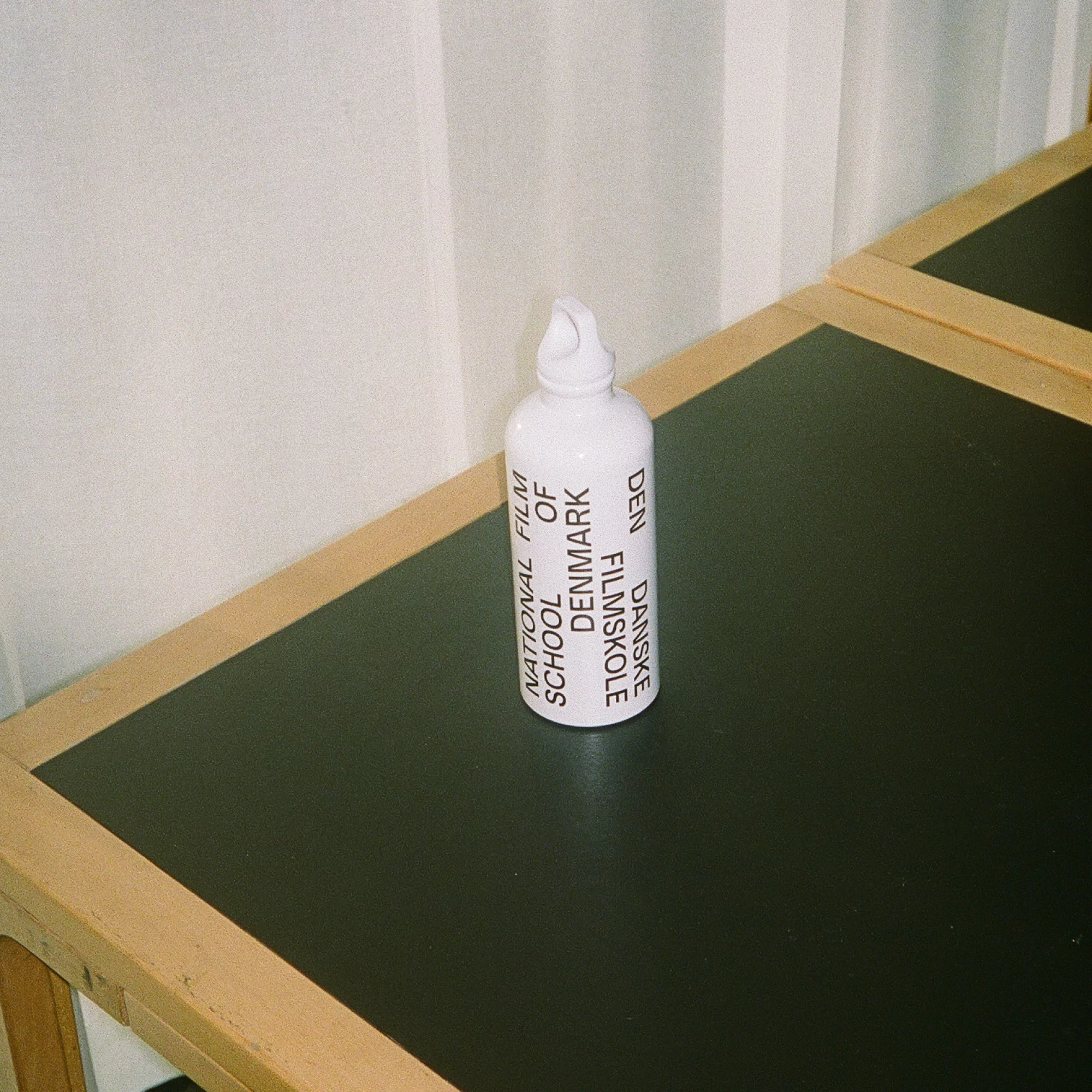 Close-up studio shot of a white water bottle with black text on a black table with a white wall background, minimalistic composition.