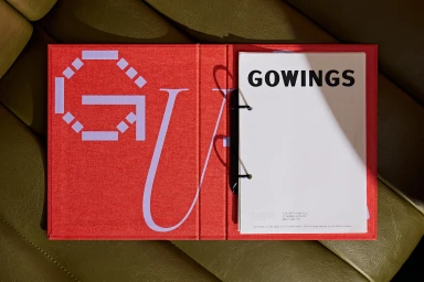 Red binder featuring geometric branding and white printed pages resting on an olive green leather surface