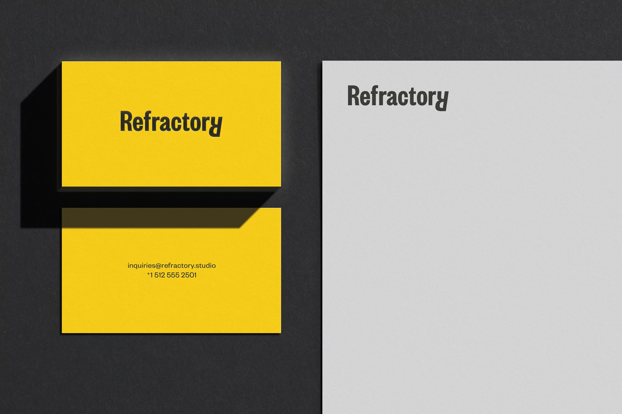Two yellow business cards and a white letterhead with black text, displayed on a dark gray surface, showcasing minimalist design.