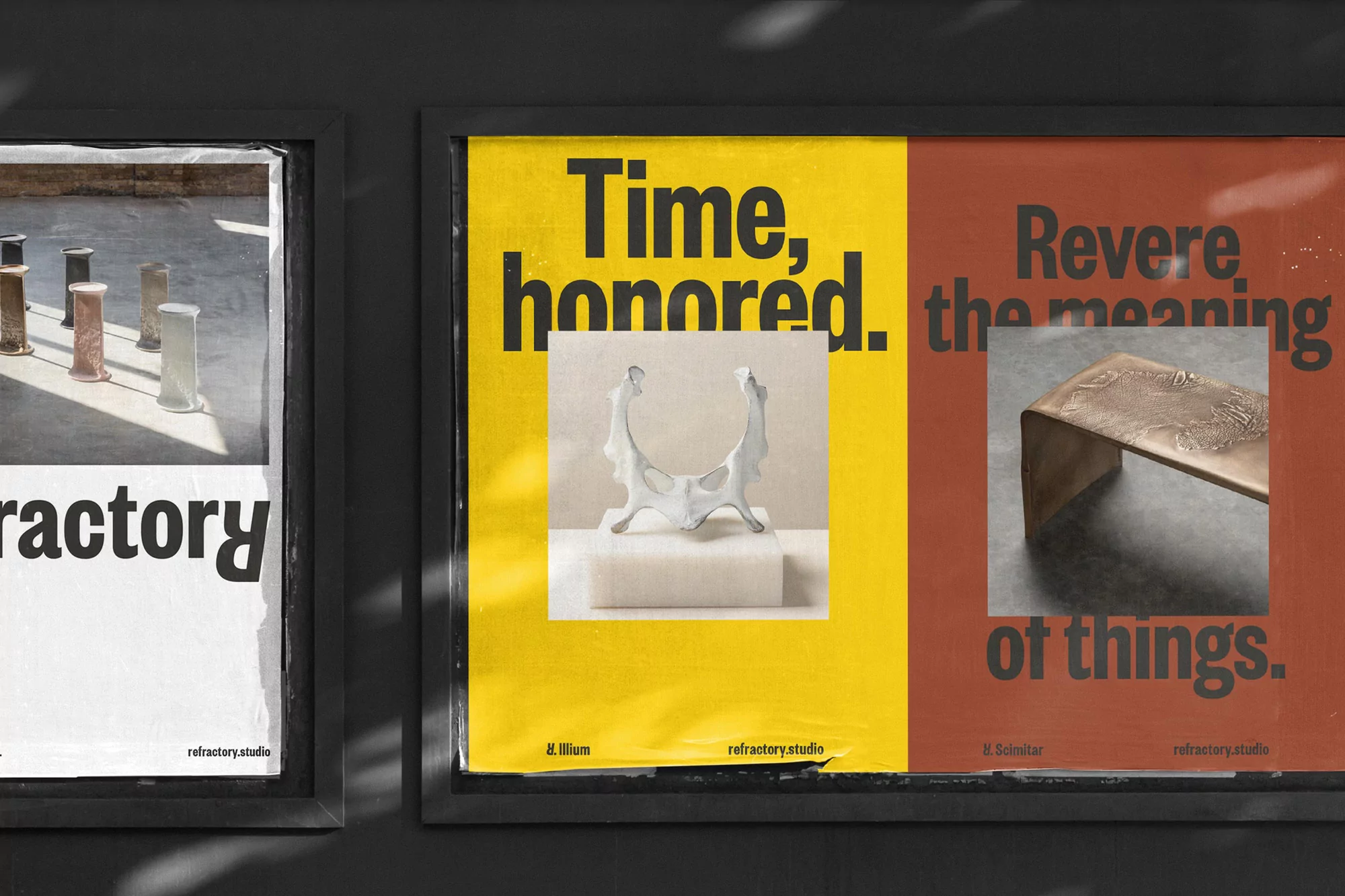 Two framed promotional posters on a grey wall: one with cylindrical objects, another with an abstract sculpture and bronze bench.
