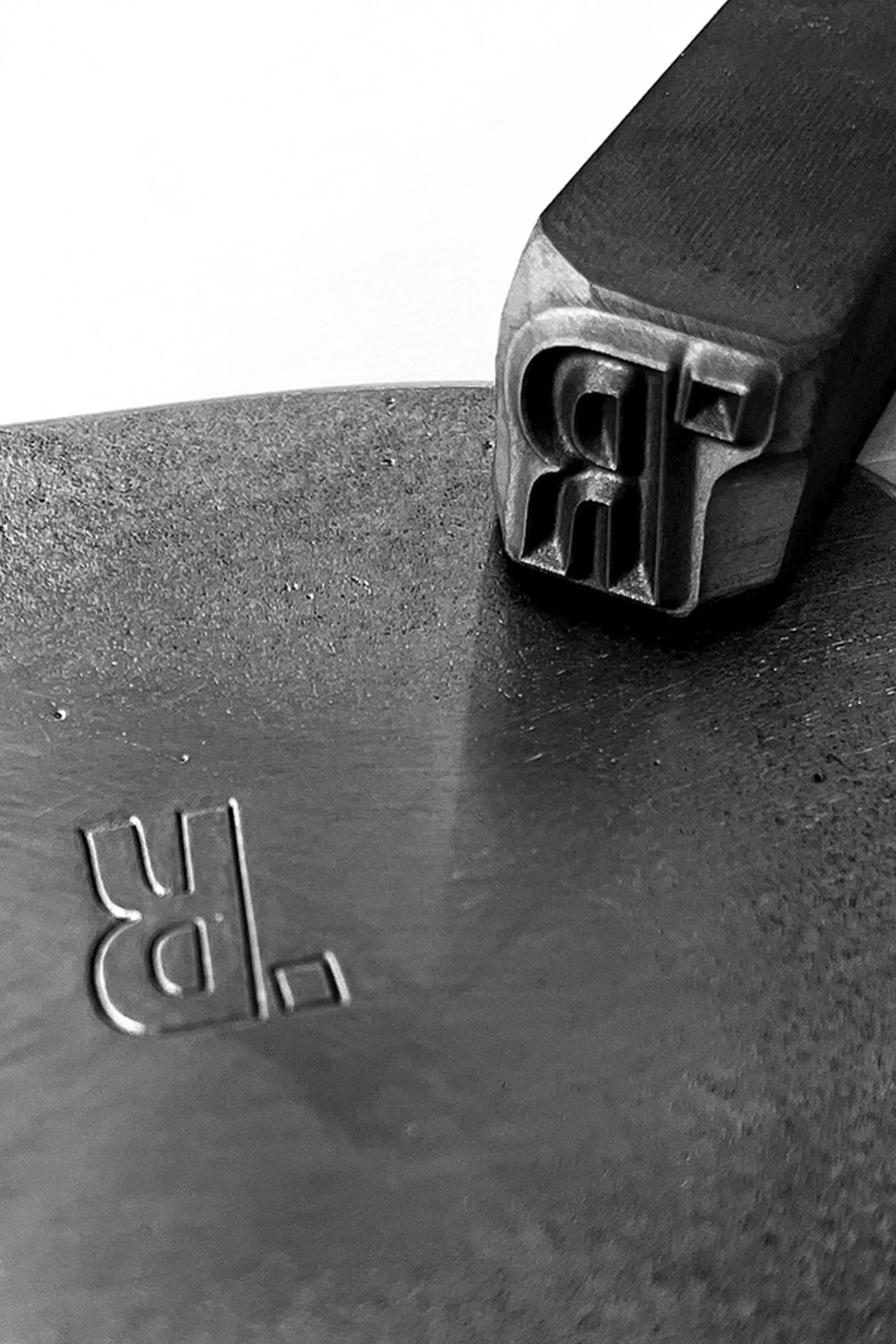 Metalworking closeup of a forged letter 'R' with a stamping tool, creating a graphic design with an industrial aesthetic.