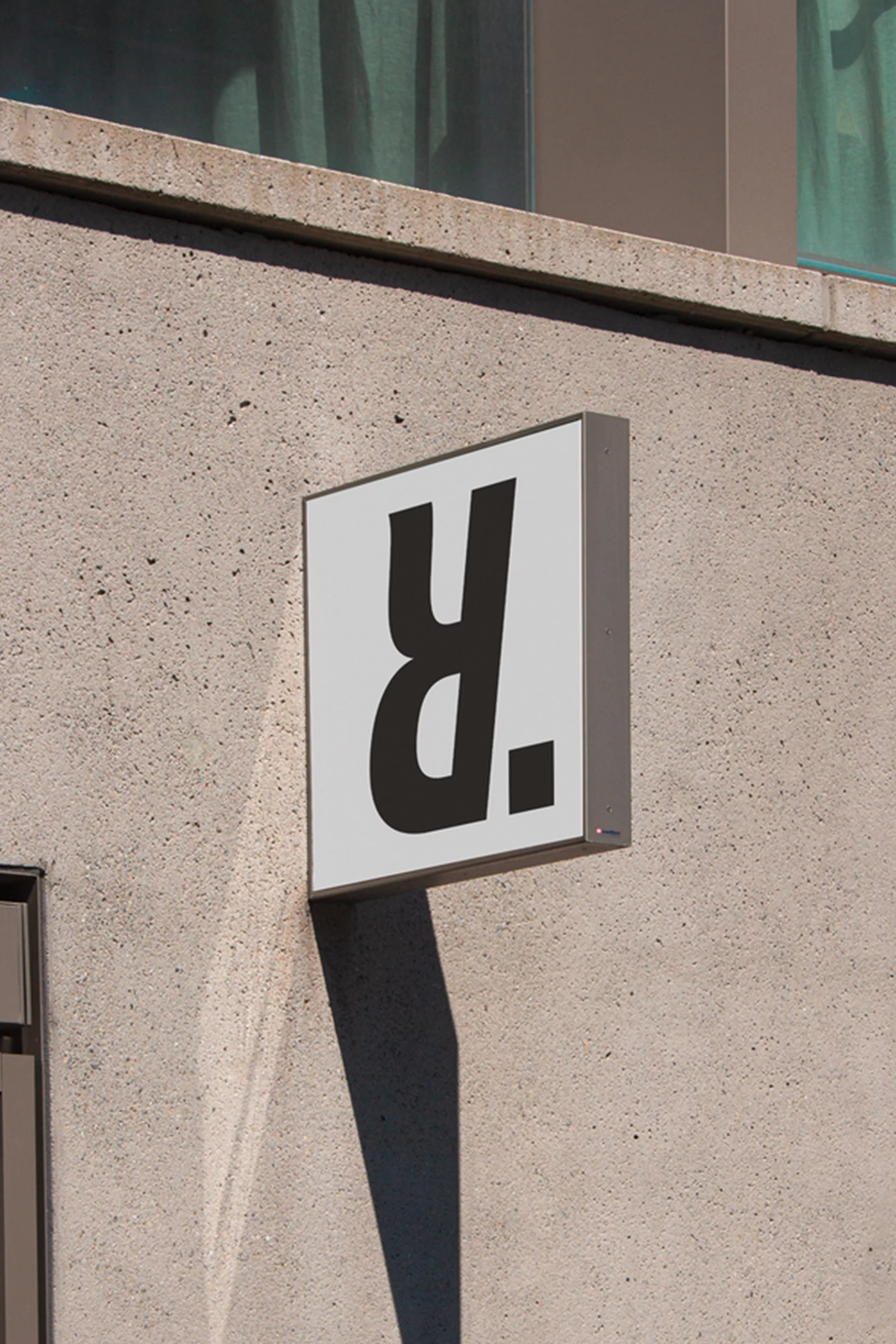 Exterior shot of a white sign on a textured concrete building with a large, stylized black 'R' and a square mark.