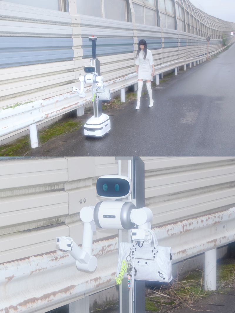 Woman in white ensemble and white boots standing alongside a white robot on an outdoor pedestrian walkway with a tall wall.