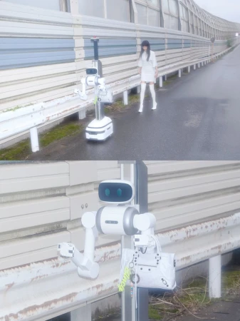Woman in white ensemble and white boots standing alongside a white robot on an outdoor pedestrian walkway with a tall wall.