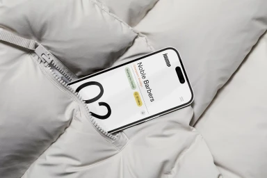 A smartphone tucked into the zippered pocket of an off-white quilted puffer jacket showing brand interface.
