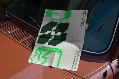 Folded printed poster with green and dark geometric graphics placed on the hood of a brown car