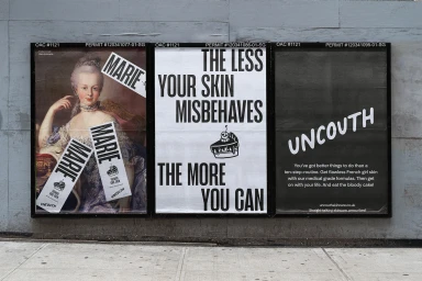 Three black poster frames mounted on a grey wooden wall displaying advertising posters for Uncouth skincare branding.
