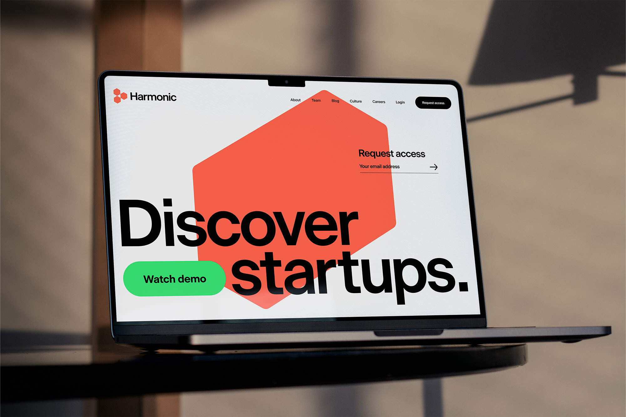 Laptop on a dark table displays the 'Harmonic' website with a geometric design, call to action, and legible UI elements in a brightly lit space.