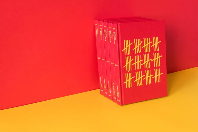 Stack of red hardcover books with tally mark design on a yellow and red surface. Close-up studio shot, colorful minimalist aesthetic.