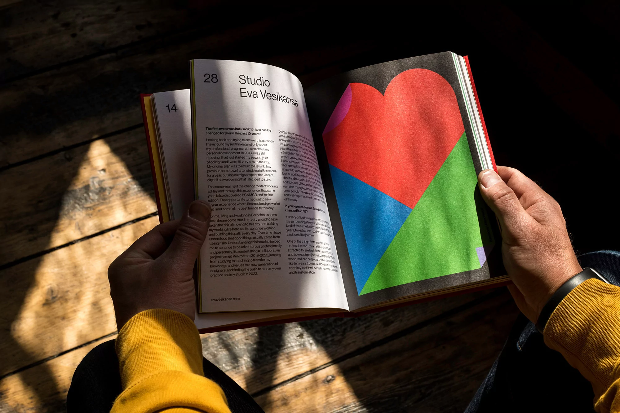 Person reading a magazine with colorful graphic design in natural light, casting a warm shadow on wood floor.