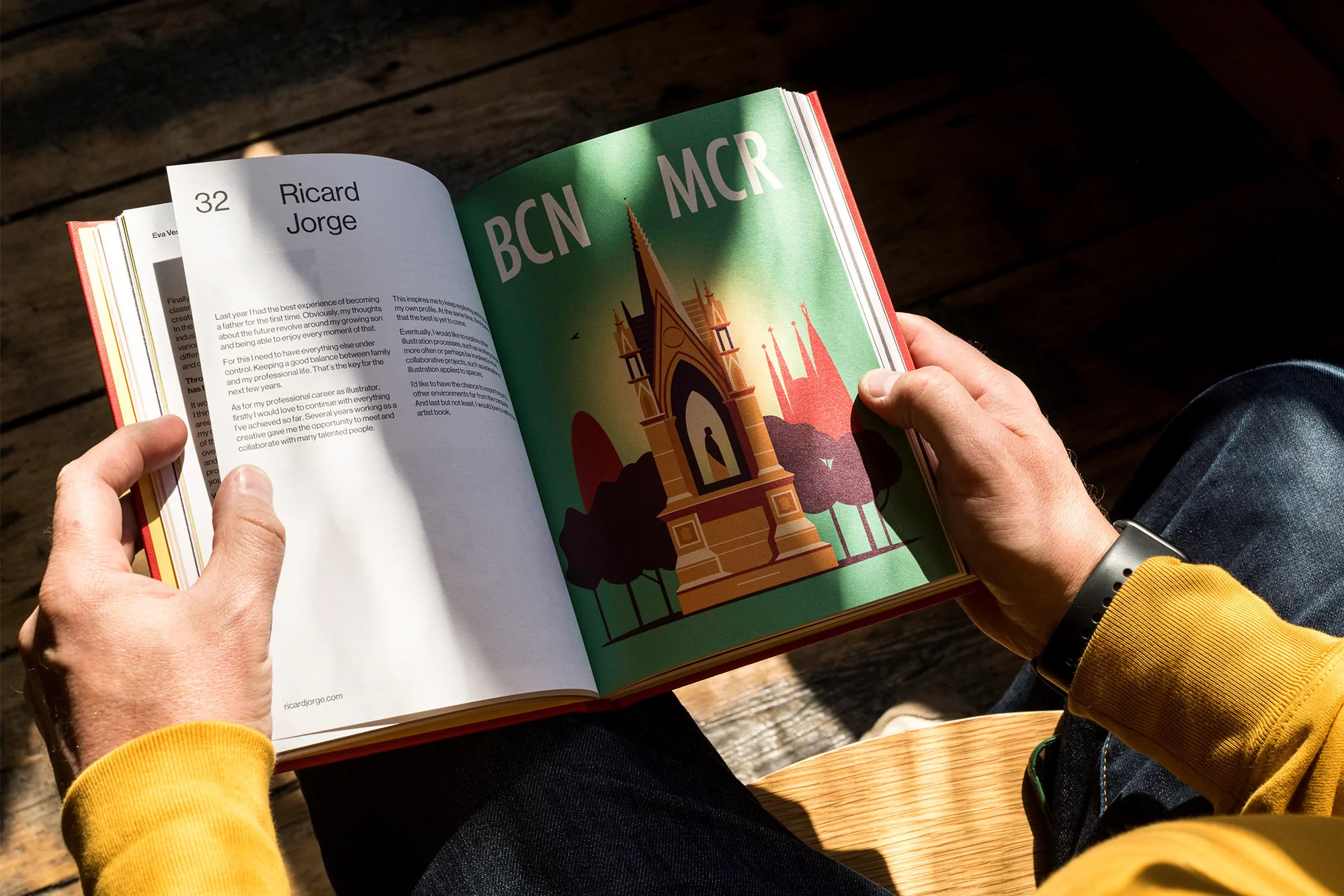 Person reading a book featuring an illustration of a cathedral, with the letters BCN and MCR on the page in warm sunlight indoors.