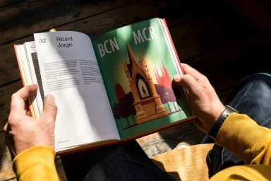 Person holding an open book featuring typographic layouts and illustration against a wooden background