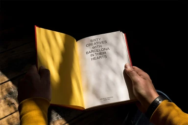 Person holding an open hardcover book displaying bold typography on the inner page under dappled natural light