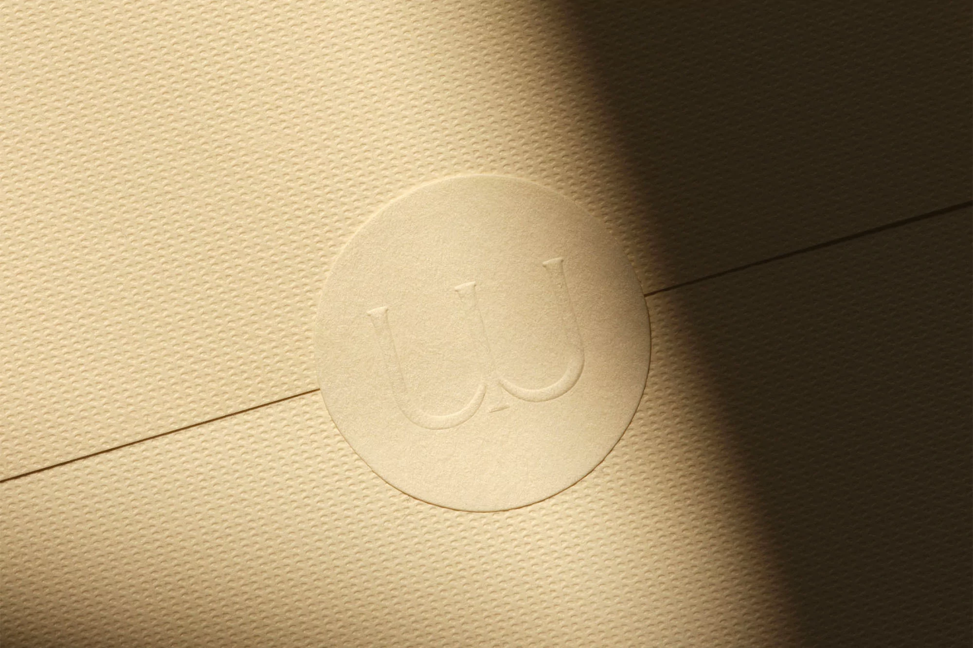 Close-up of a textured, beige envelope with an embossed circular seal, partially lit by natural light creating soft shadows.
