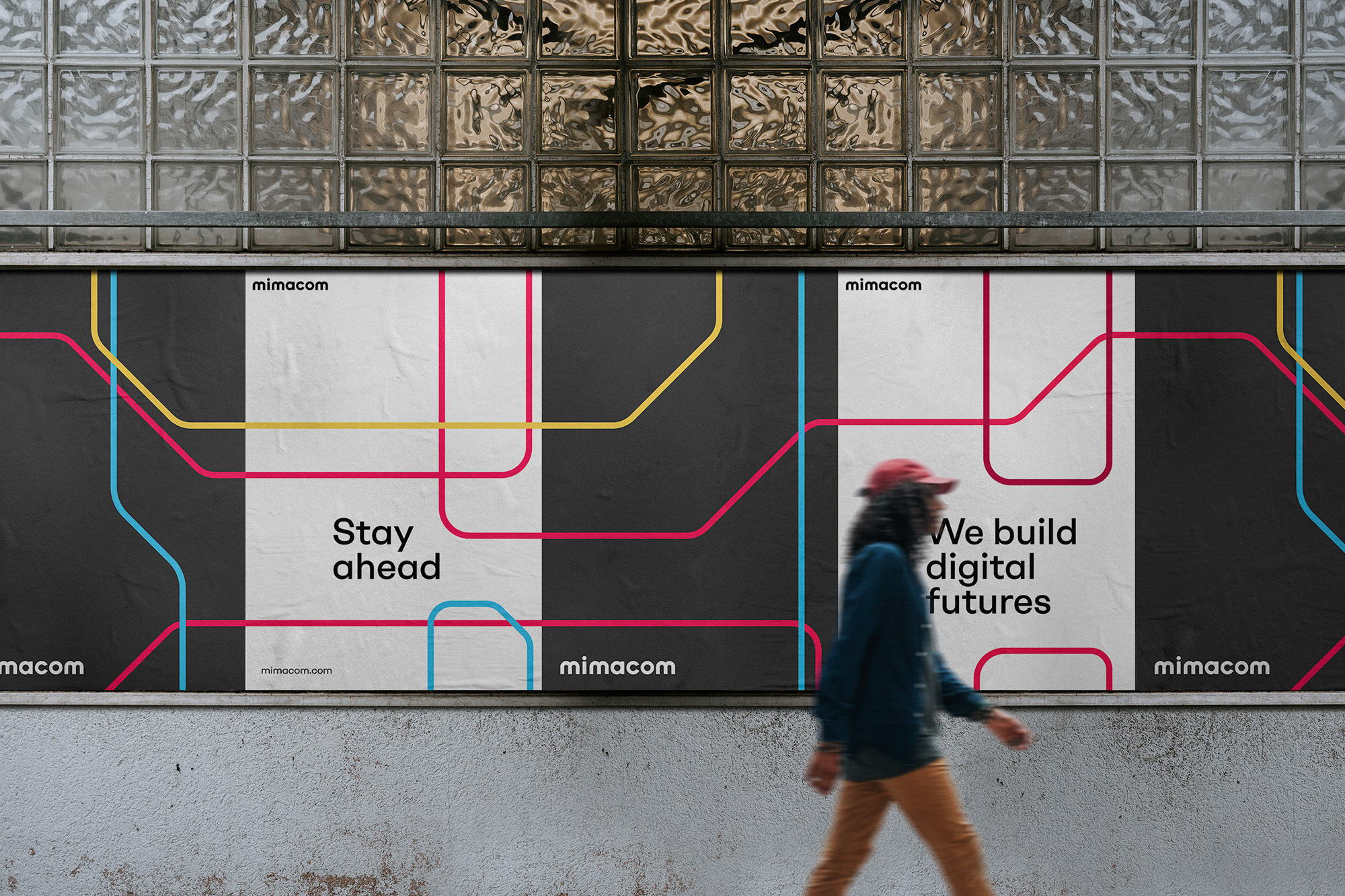 An abstract Mimacom advertising poster is mounted to a subway wall as a person walks in front. Bright colors and bold patterns.
