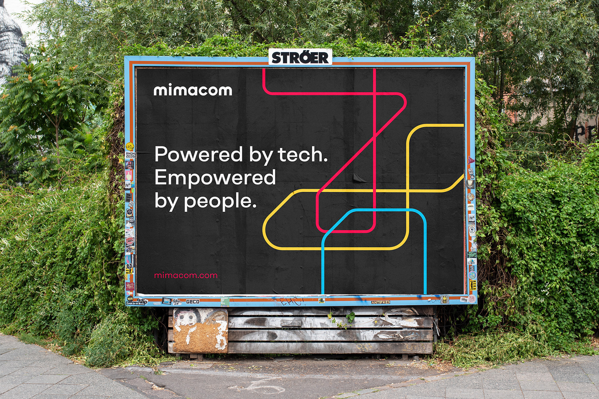 Outdoor billboard advertising mimacom with colorful graphic lines and the tagline 'Powered by tech. Empowered by people.' in daytime.