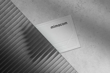 Mimacom brand identity graphic design featuring a logo card on a textured concrete and fluted surface.