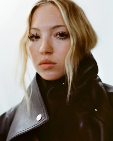 Close-up portrait of a young adult woman with blonde hair wearing a black leather jacket against a plain white background.