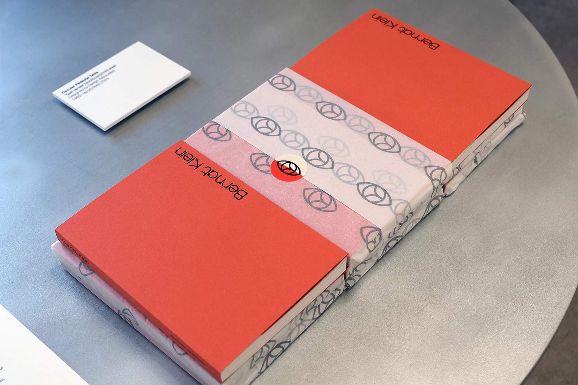 Two coral-covered books by Bernat Klein are wrapped in patterned paper on a gray table, accompanied by a white card.