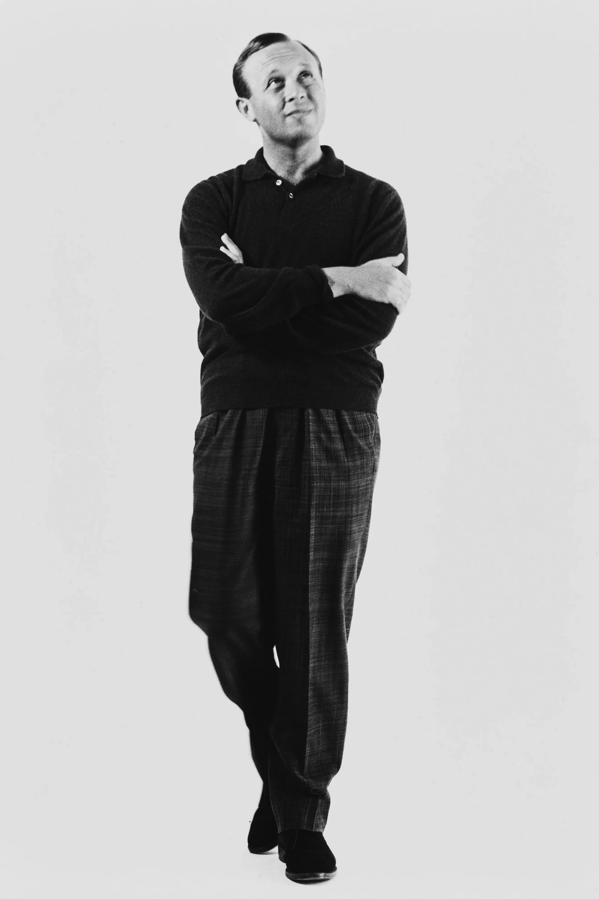 Black and white portrait of a man standing with arms crossed against a plain light background