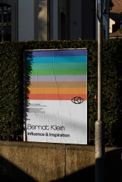 Printed poster for Bernat Klein Influence and Inspiration featuring colourful horizontal stripes mounted on a stone wall.