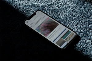 Smartphone displaying a journal webpage resting on a textured dark surface with angled hard light