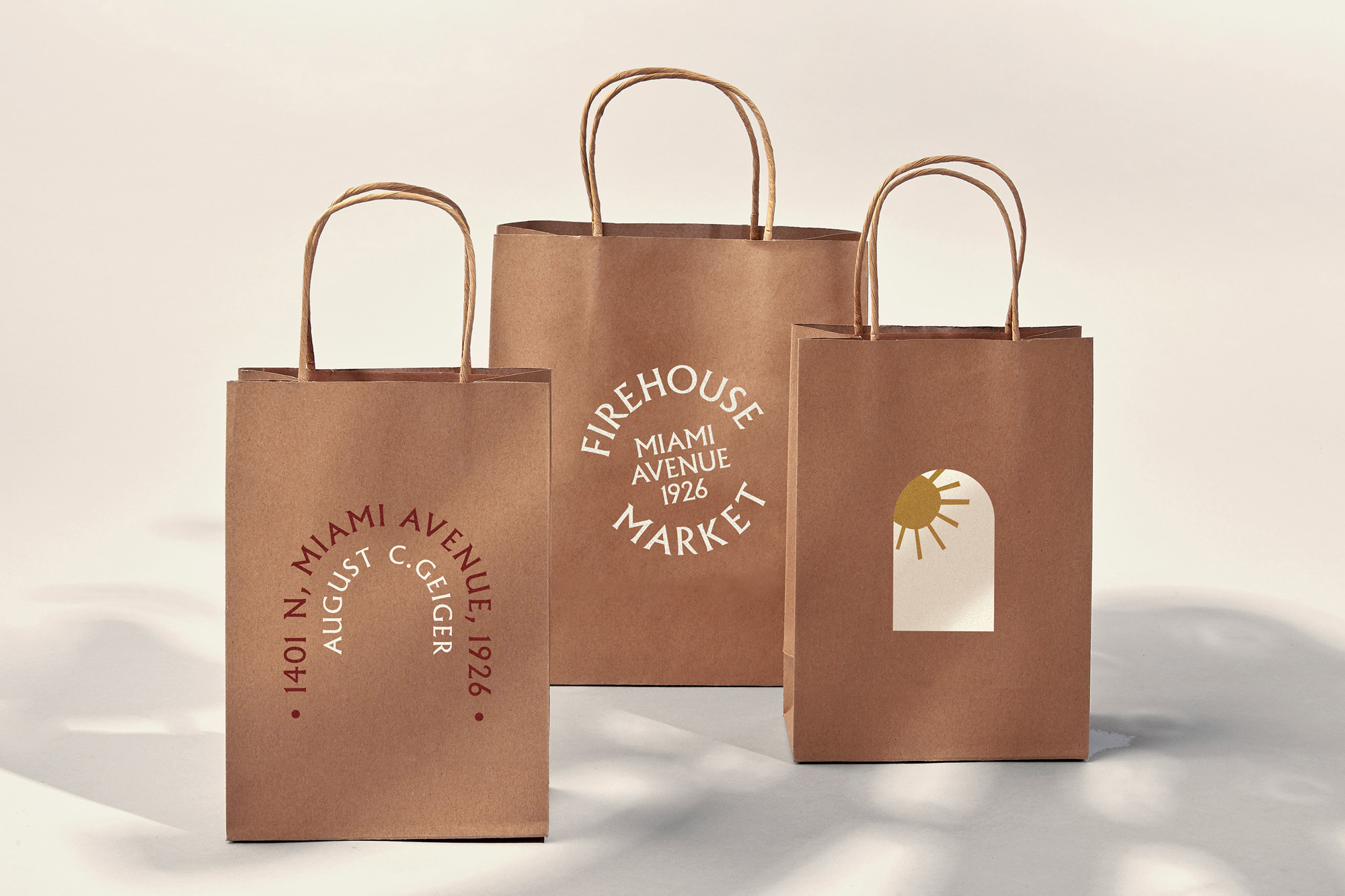 Three brown paper shopping bags with minimalist branding, showcasing logo and text designs in a bright studio setting.