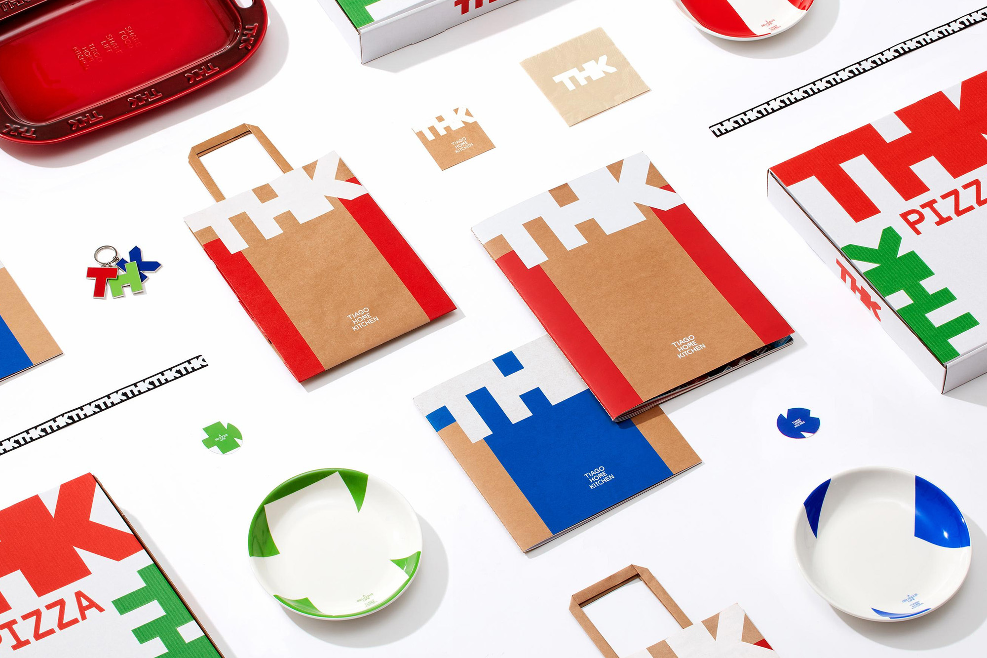 Overhead shot of THK branded pizza boxes, plates, and bags in red, white, green, and blue on a white surface showcasing food industry branding.