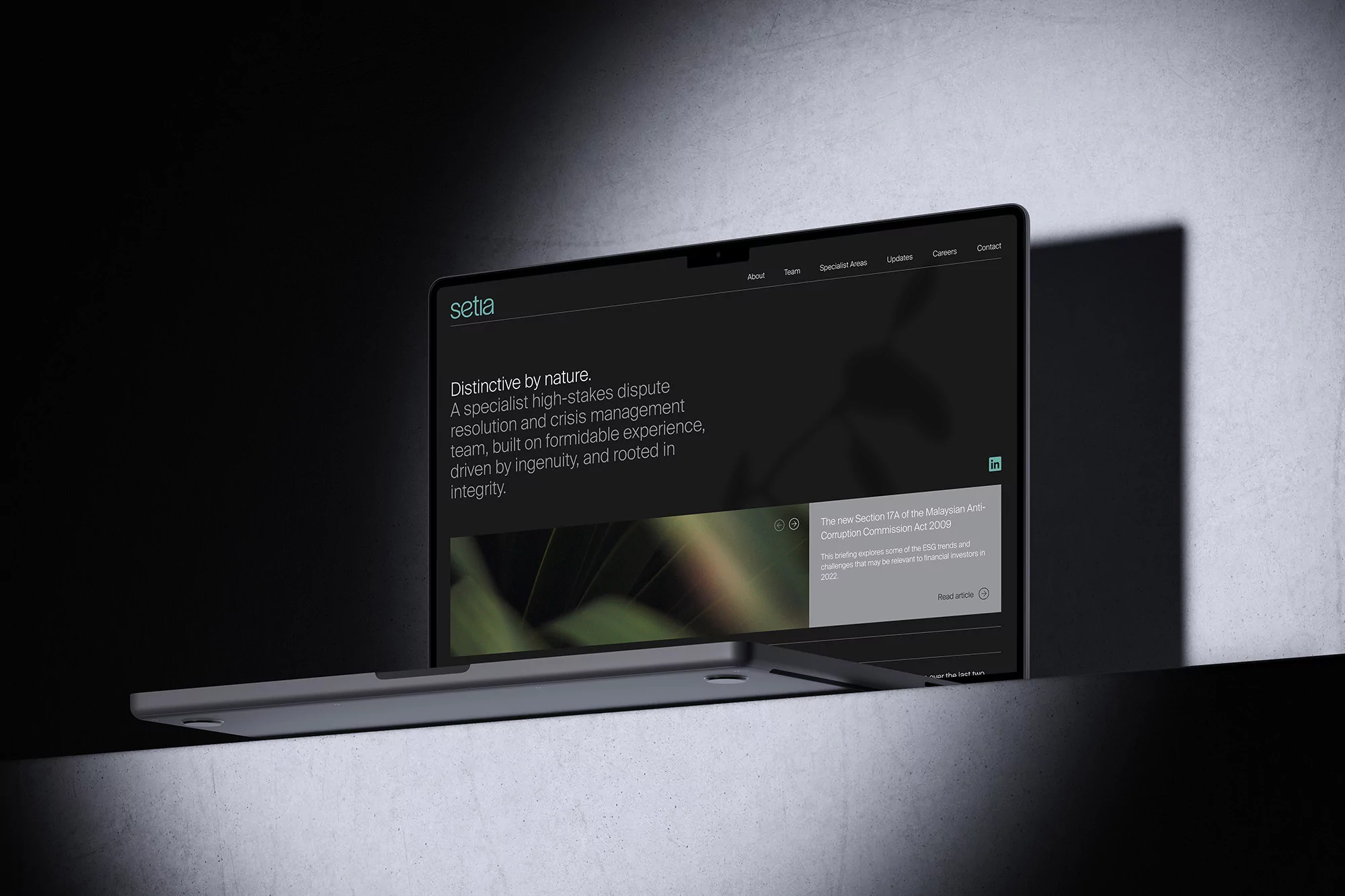Laptop displays Setia website with its mission statement and brand. The composition has a sleek, corporate aesthetic in a dark and indoor setting.