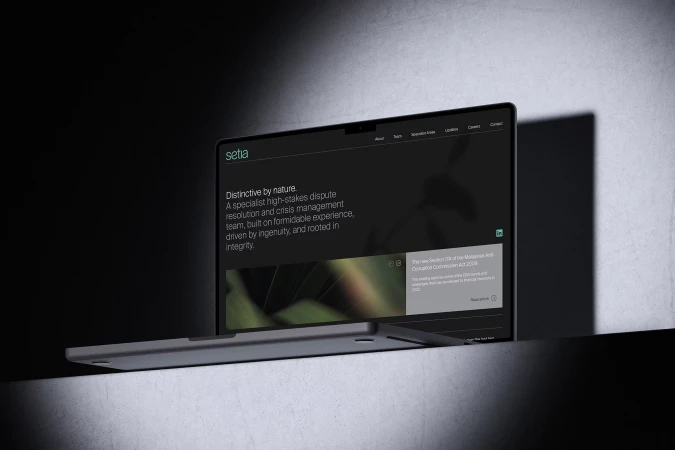 Laptop displays Setia website with its mission statement and brand. The composition has a sleek, corporate aesthetic in a dark and indoor setting.