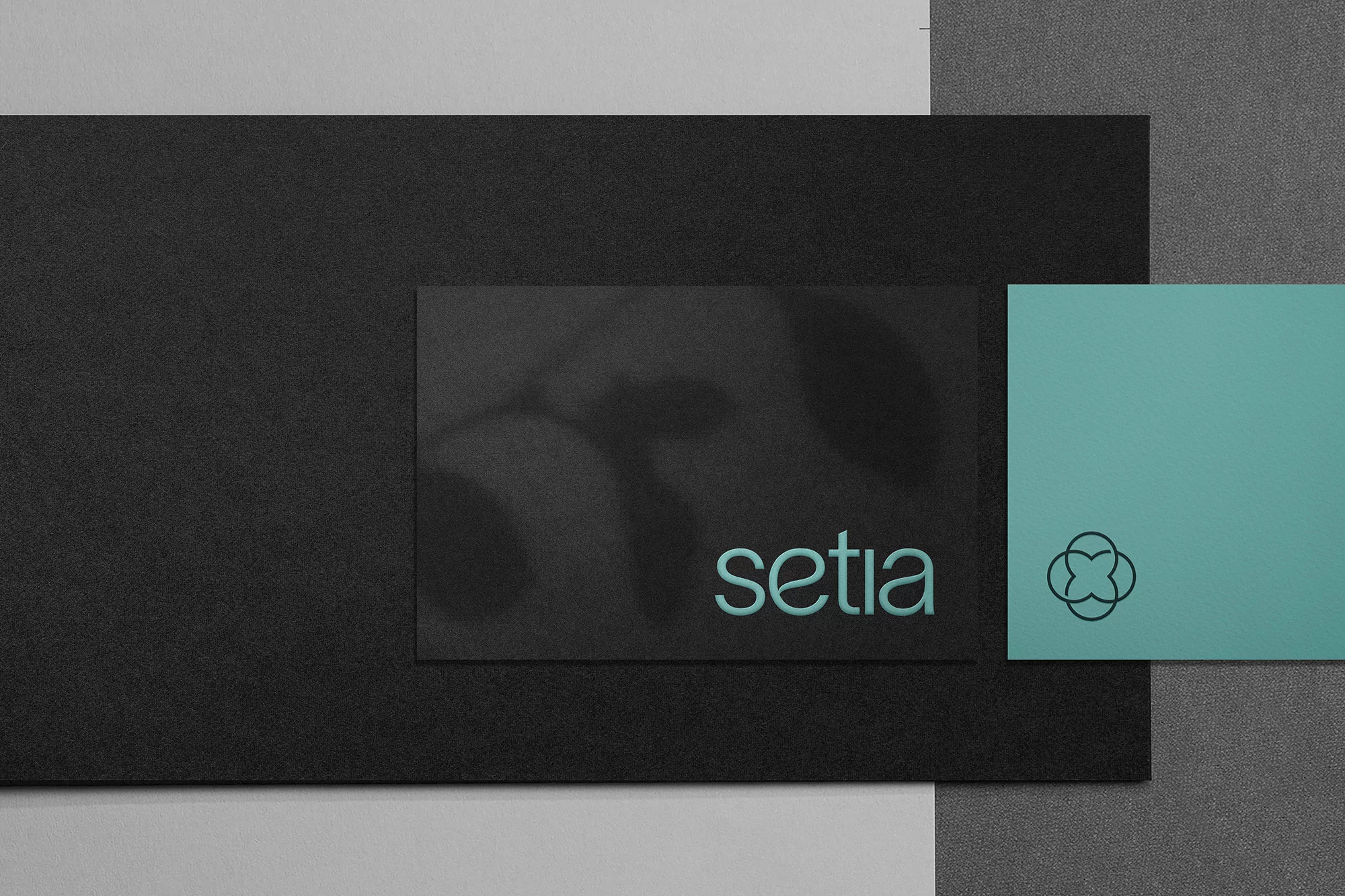 Elevated shot of black, grey, and teal cards with the word 'setia' and a clover logo displayed against textured backgrounds.