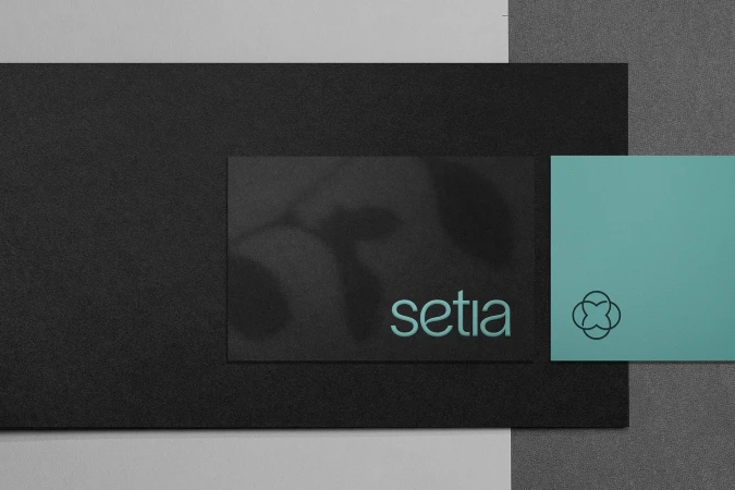 Elevated shot of black, grey, and teal cards with the word 'setia' and a clover logo displayed against textured backgrounds.
