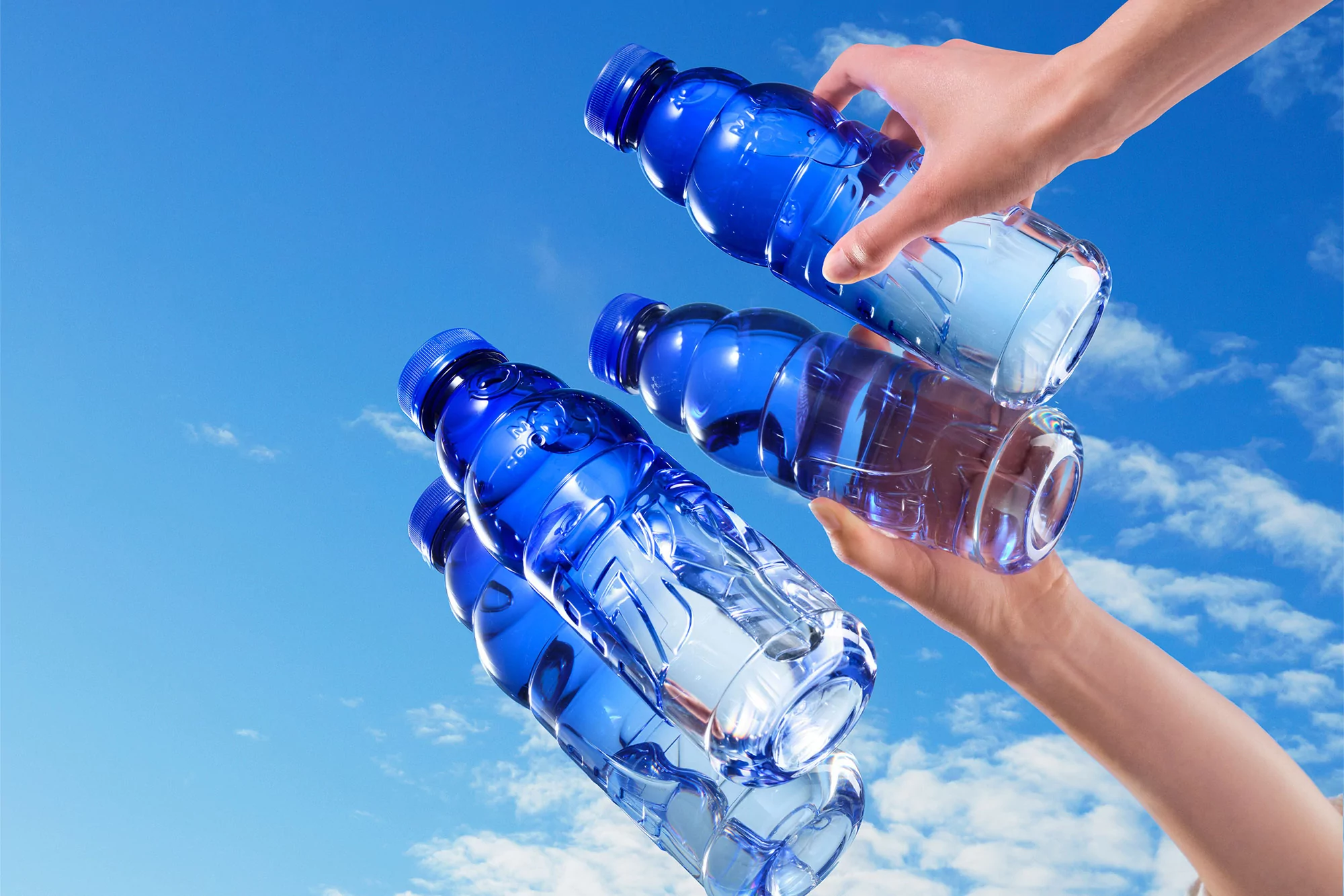 Hands holding blue plastic water bottles in clear sky. Refreshment and hydration concept. Summer outdoor scene. Beverage marketing visuals.