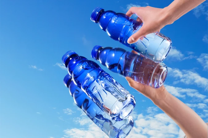 Hands holding blue plastic water bottles in clear sky. Refreshment and hydration concept. Summer outdoor scene. Beverage marketing visuals.