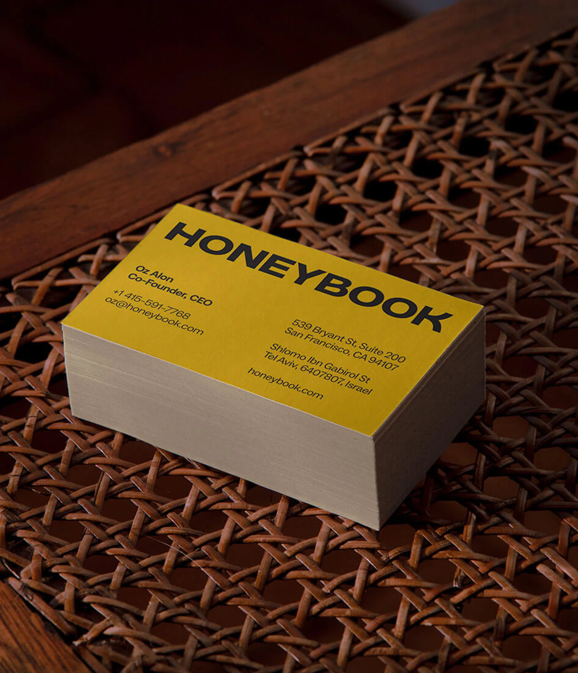Stack of yellow HoneyBook business cards on a woven brown surface. The cards display contact information including names, addresses, and URLs.