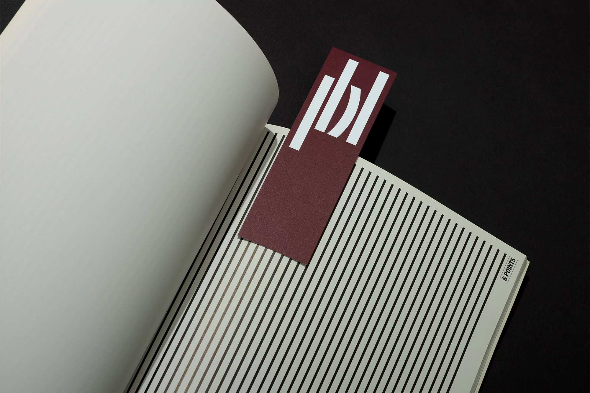 Open book with black and white striped page and a maroon bookmark with white abstract logo against a solid black background.