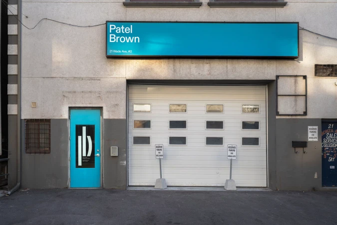 Exterior shot of an industrial building with a blue door and sign. A garage door is visible, accompanied by parking signs.