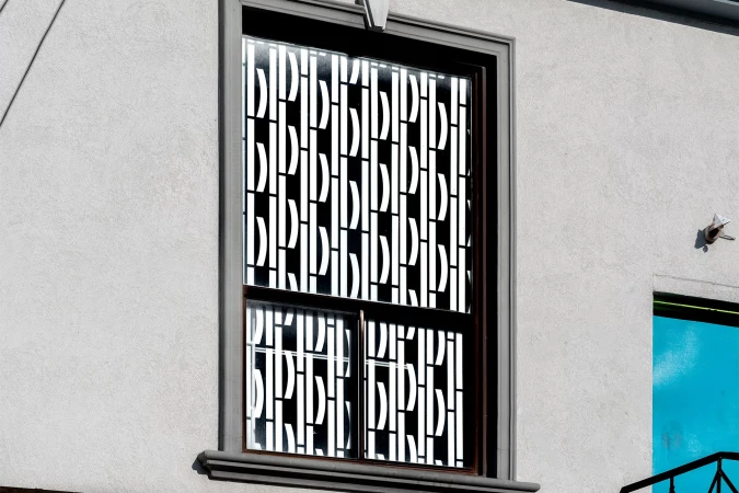 Exterior view of a modern building with a large window featuring a black frame and a decorative white and black pattern.