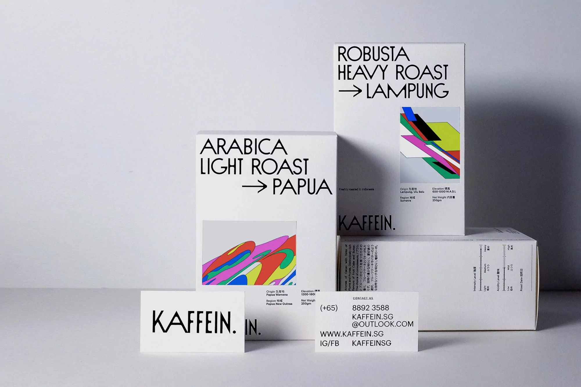 Product shot of Kaffein brand Arabica Light Roast and Robusta Heavy Roast coffee bean boxes and business card on white backdrop.