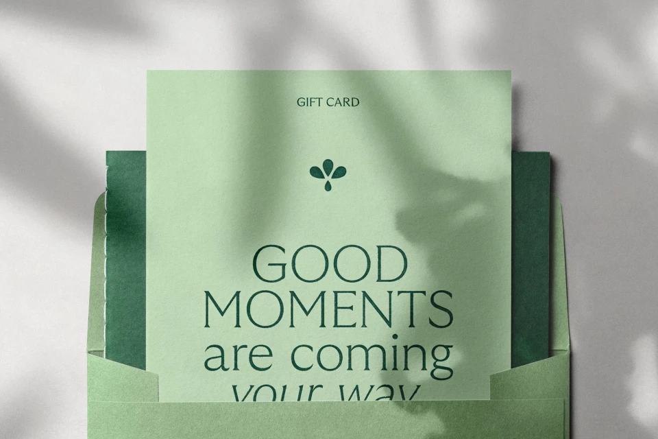 Green and white gift card with typography in an envelope, featuring stylized botanical elements and a soft shadow backdrop.