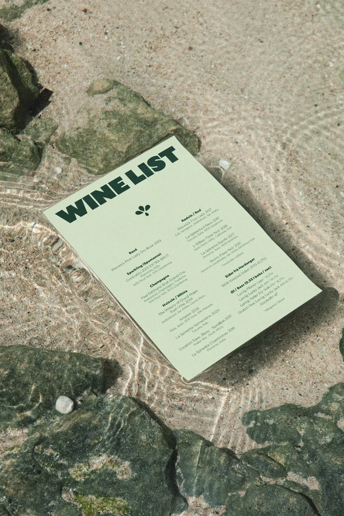 Pale green wine list menu resting on wet rocky ground near shallow water